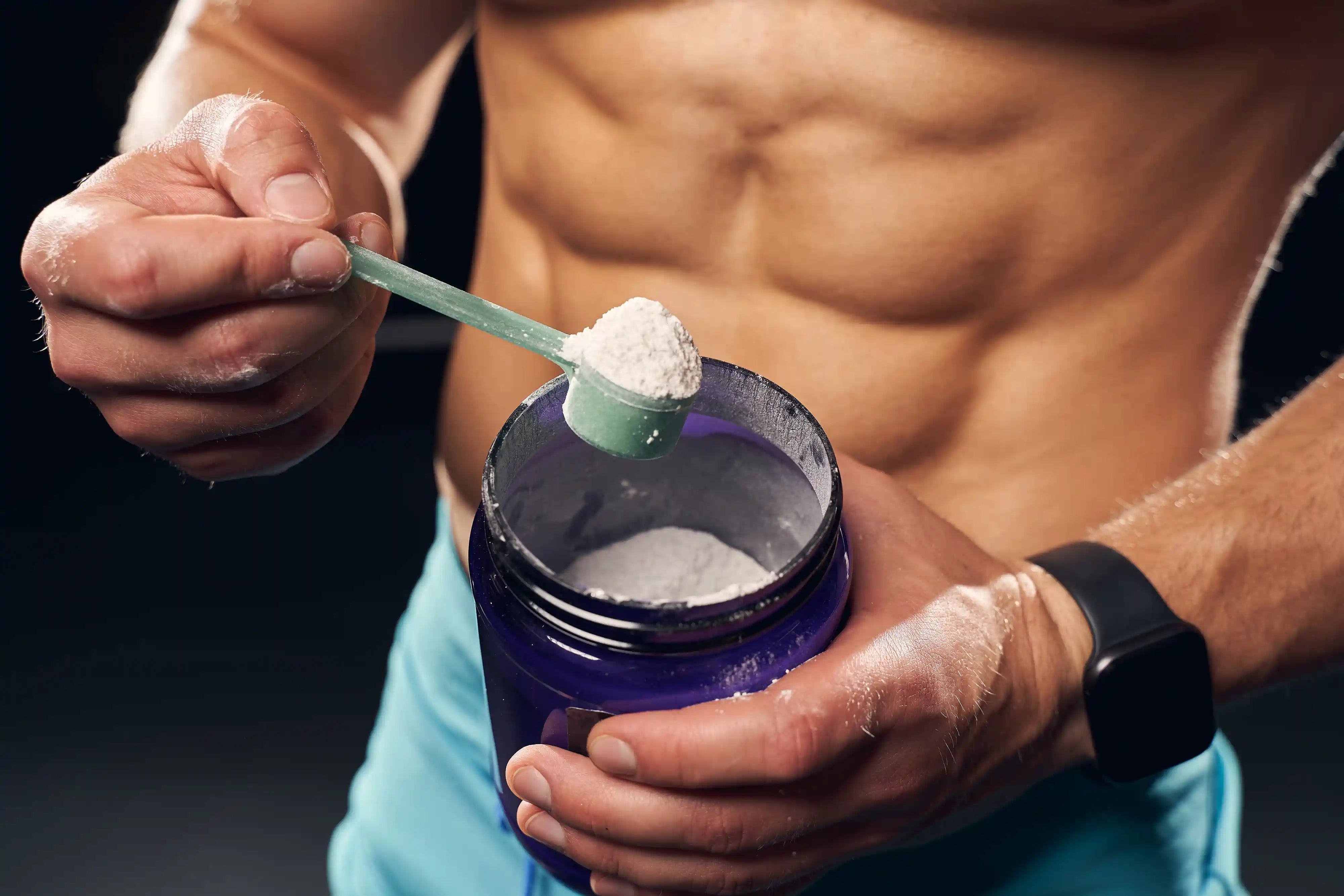 muscular man holding a jar with a scoop of creatine powder