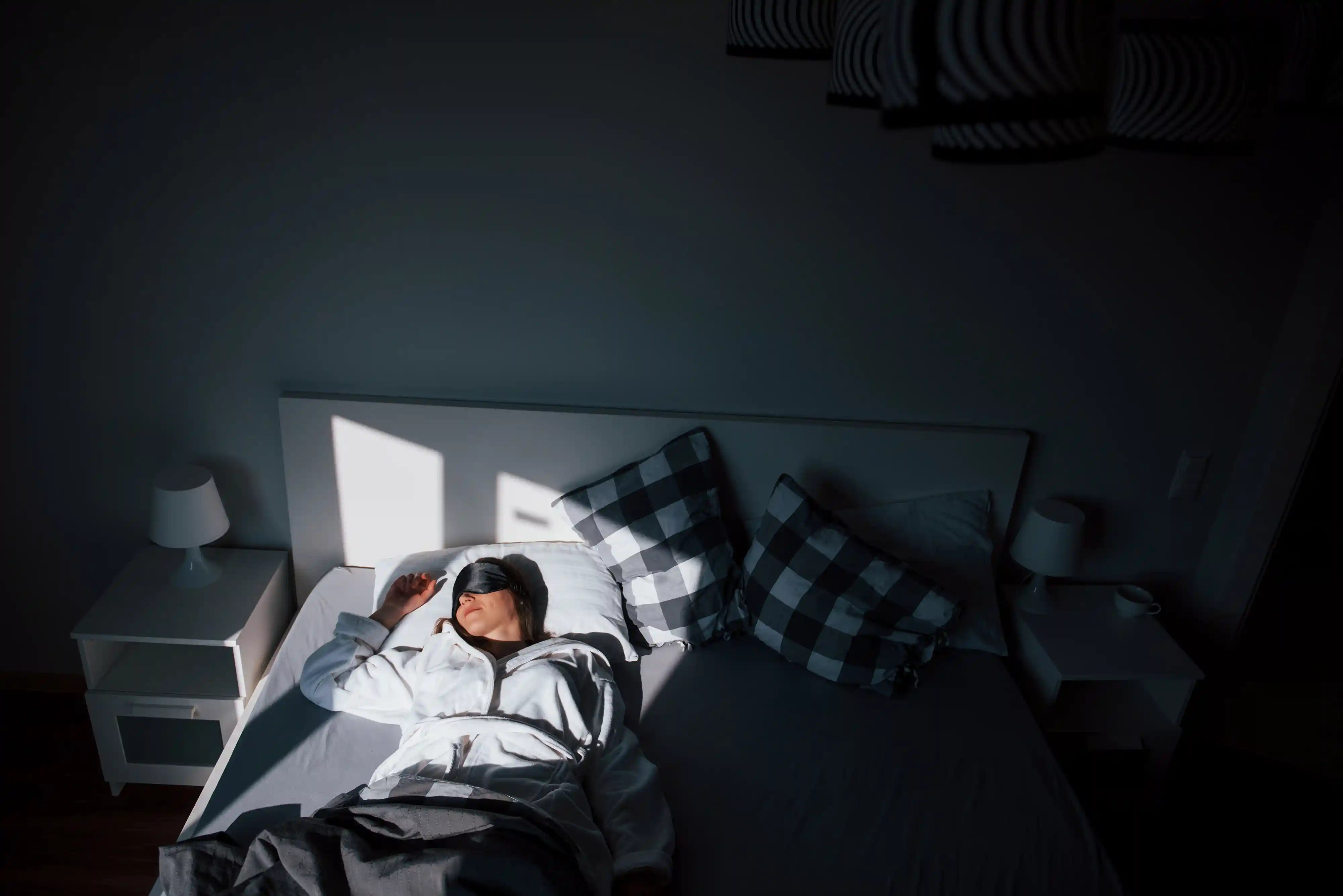 women sleeping with a mask and the sun shining through the window in a dark room
